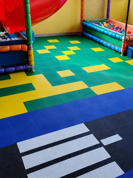 Piscina de bolinhas e escorregador sobre piso modular verde, amarelo e azul, com faixa de pedestres