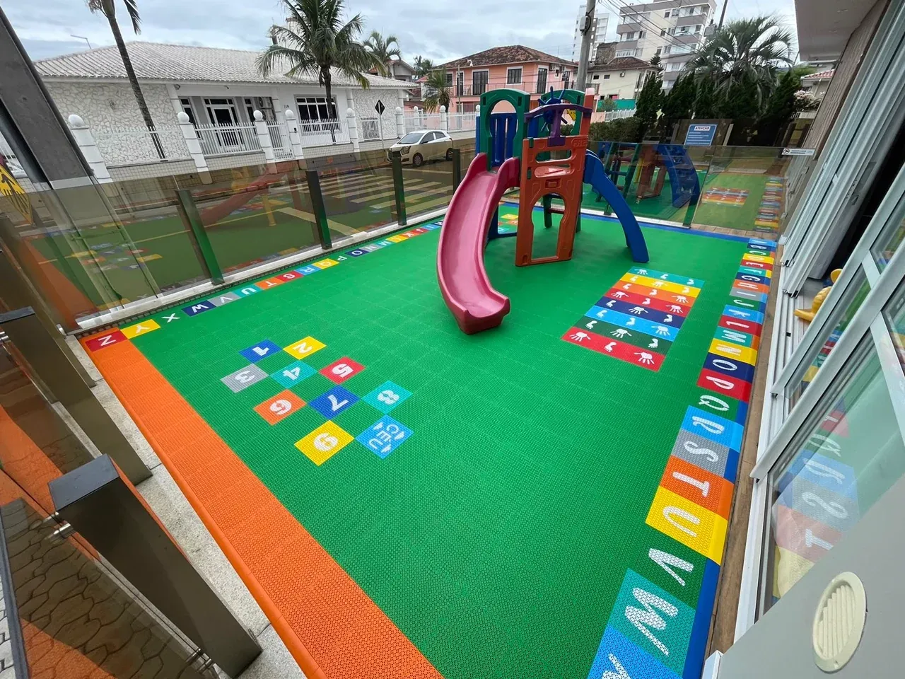 Balanços sobre piso modular verde com amarelinha ao lado